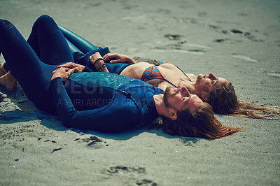 Buy stock photo Shot of a young couple relaxing after a surf at the beach