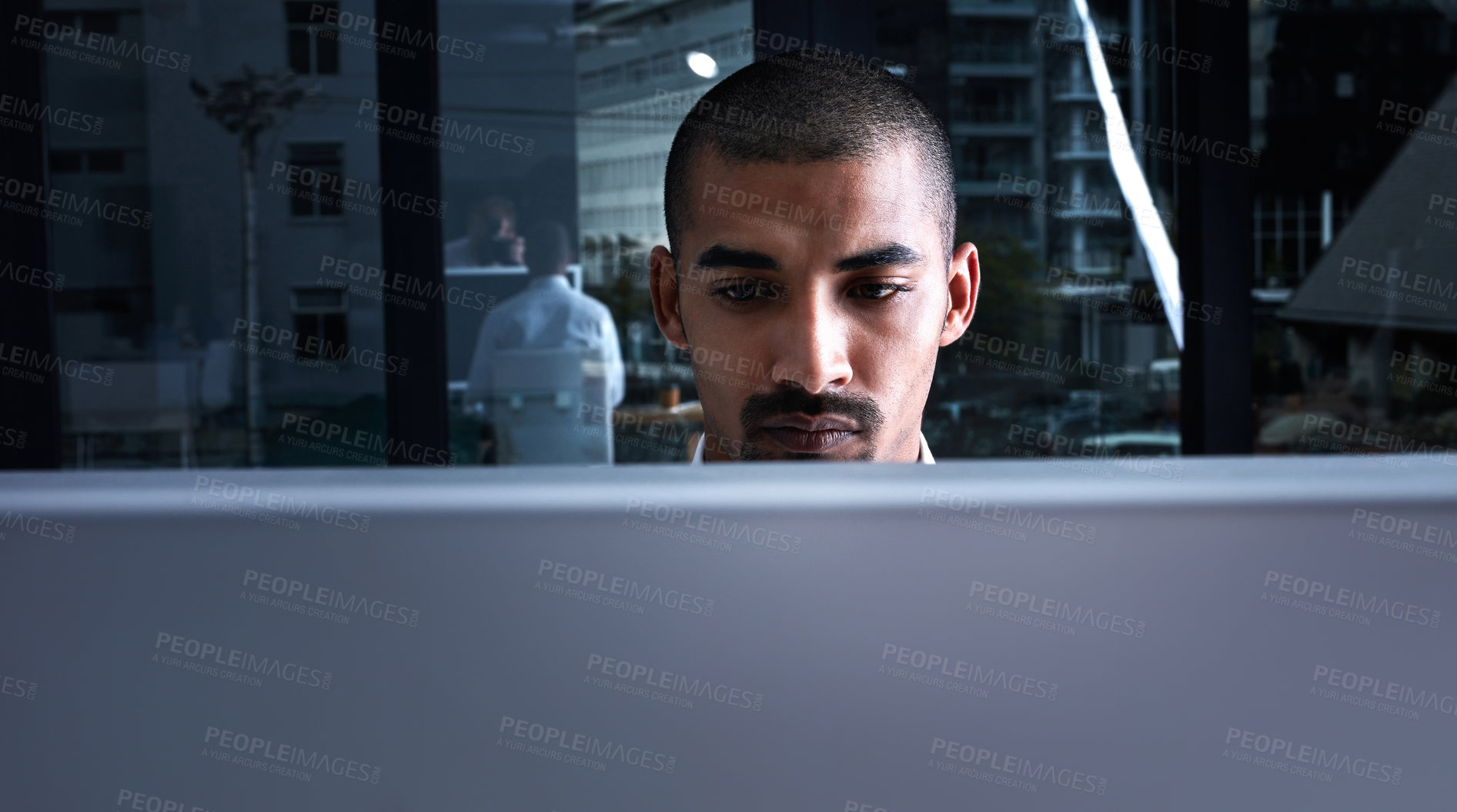 Buy stock photo Shot of a young businessman using a computer at night in a modern office