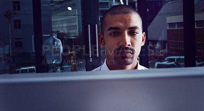 Buy stock photo Shot of a young businessman using a computer at night in a modern office