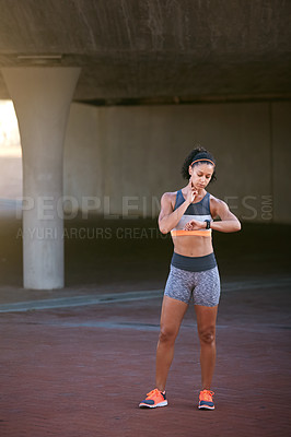 Buy stock photo Full length shot of an attractive young woman checking her heart rate during a run through the city
