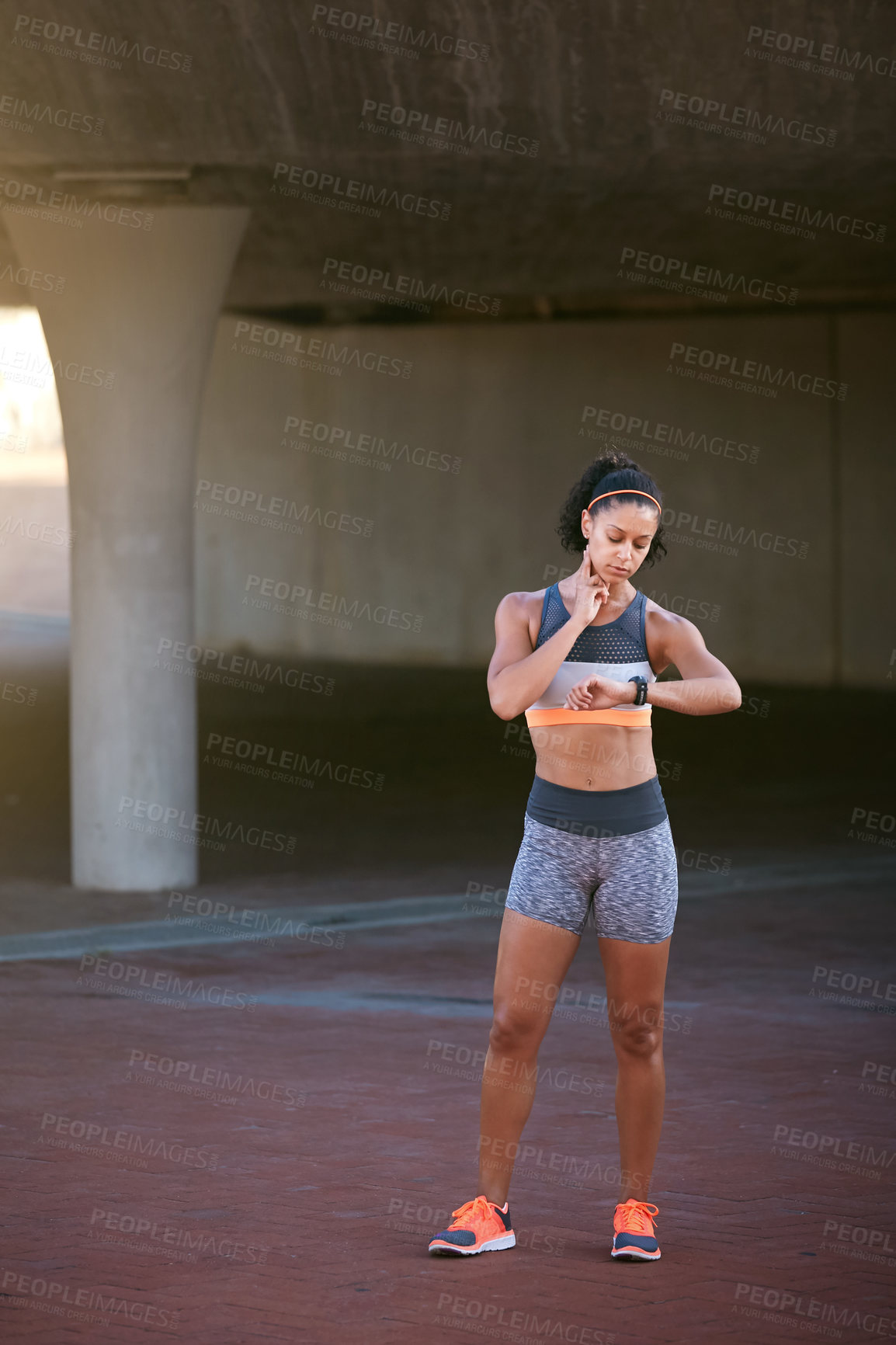 Buy stock photo Full length shot of an attractive young woman checking her heart rate during a run through the city