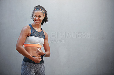 Buy stock photo Cropped shot of a sporty young woman flexing her arms in front of a grey wall