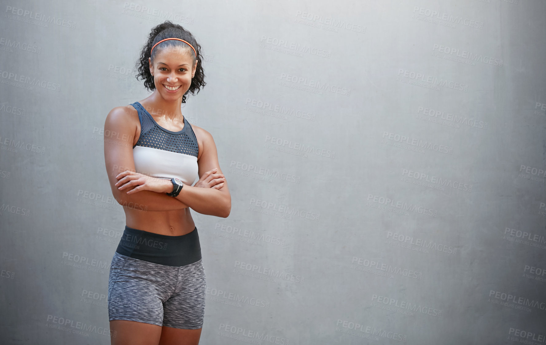 Buy stock photo Cropped portrait of a sporty young woman standing with her arms folded in front of a grey wall