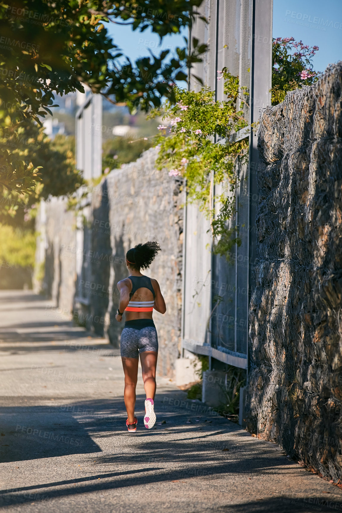 Buy stock photo Rearview shot of an unrecognizable young woman taking a run through the city