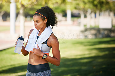 Buy stock photo Shot of a sporty young woman drinking water while exercising outside