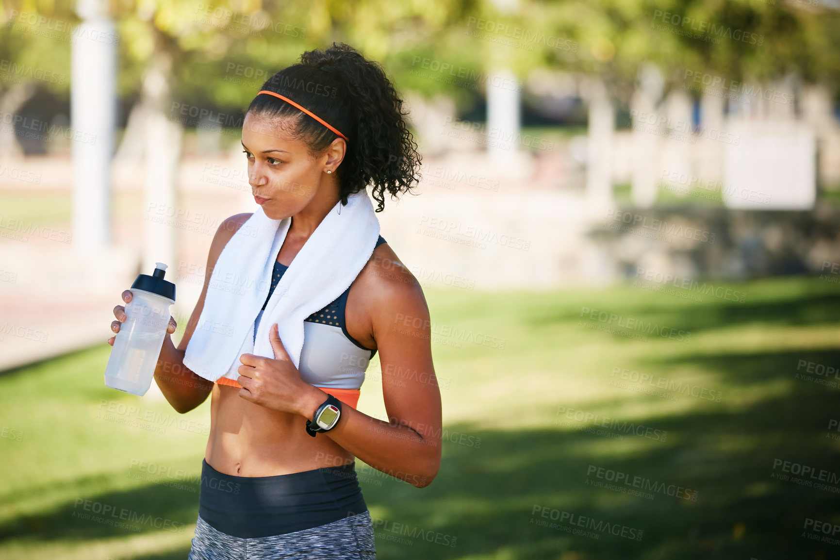Buy stock photo Shot of a sporty young woman drinking water while exercising outside