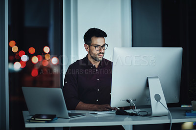 Buy stock photo Shot of a young businessman using a computer at his desk during a late night at work