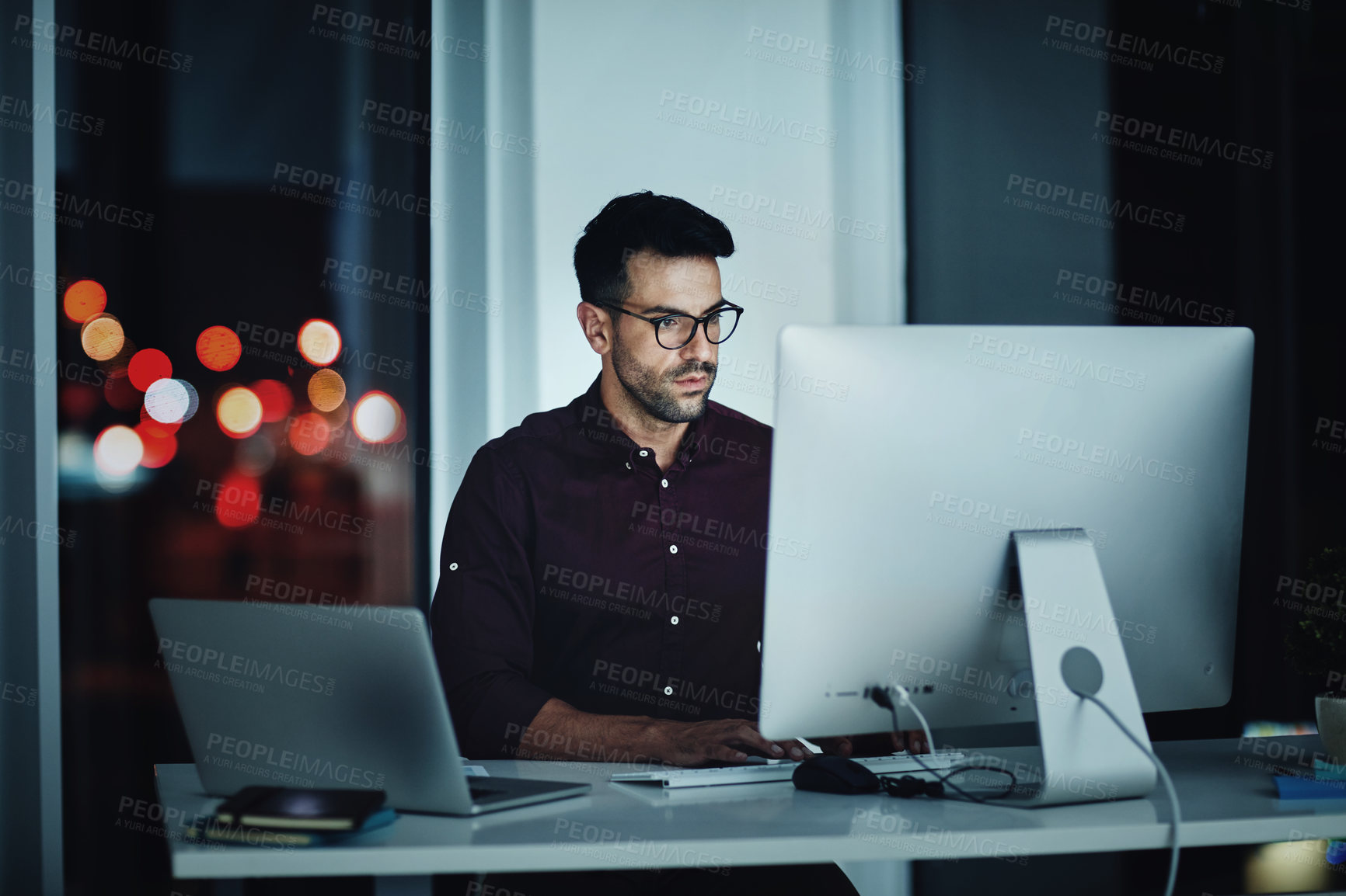 Buy stock photo Shot of a young businessman using a computer at his desk during a late night at work