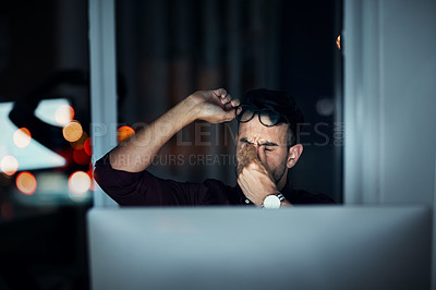 Buy stock photo Shot of a young businessman feeling exhausted while working at his desk during a late night at work