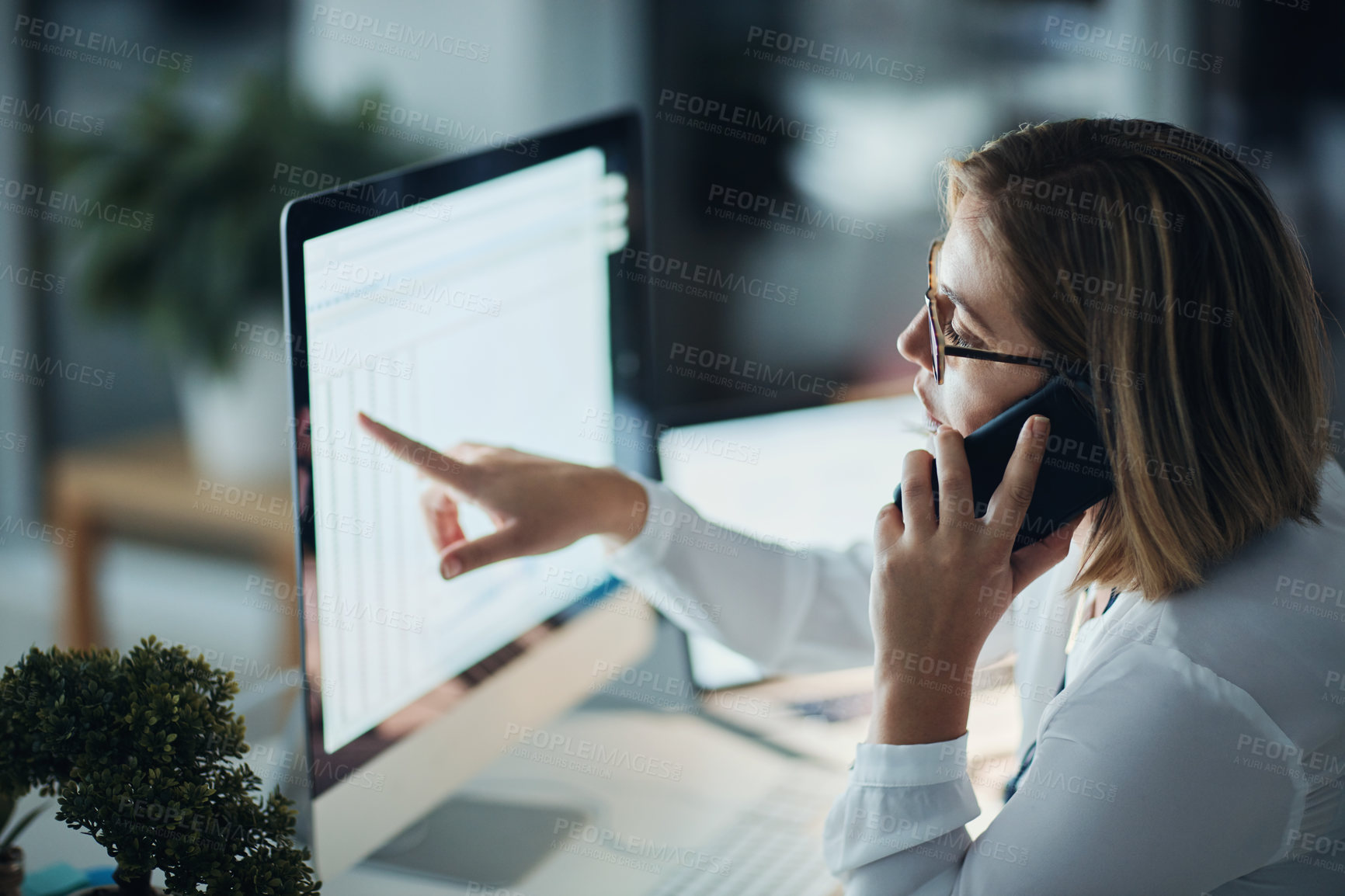 Buy stock photo Shot of a businesswoman using a computer and talking on the phone during a late night at work