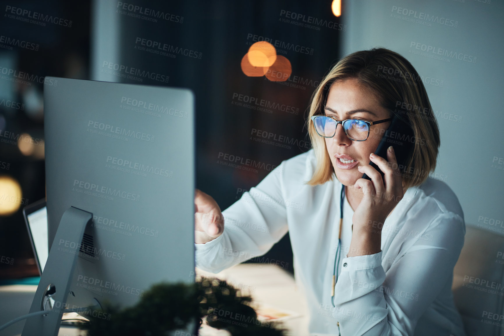 Buy stock photo Shot of a businesswoman using a computer and talking on the phone during a late night at work