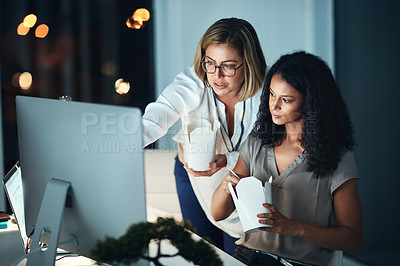 Buy stock photo Shot of two colleagues using a computer together and eating takeout during a late night at work