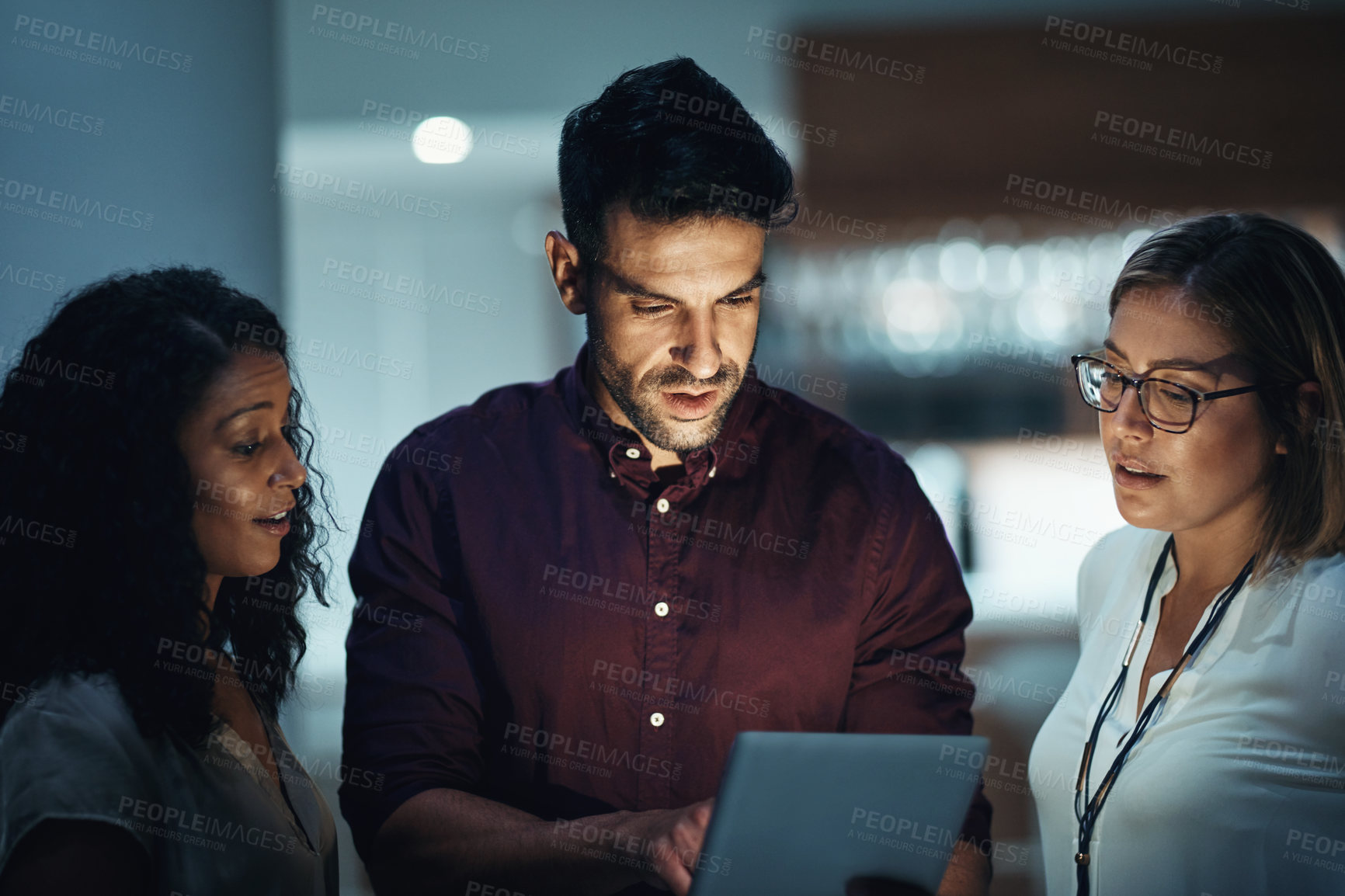 Buy stock photo Shot of a group of colleagues using a digital tablet together during a late night at work