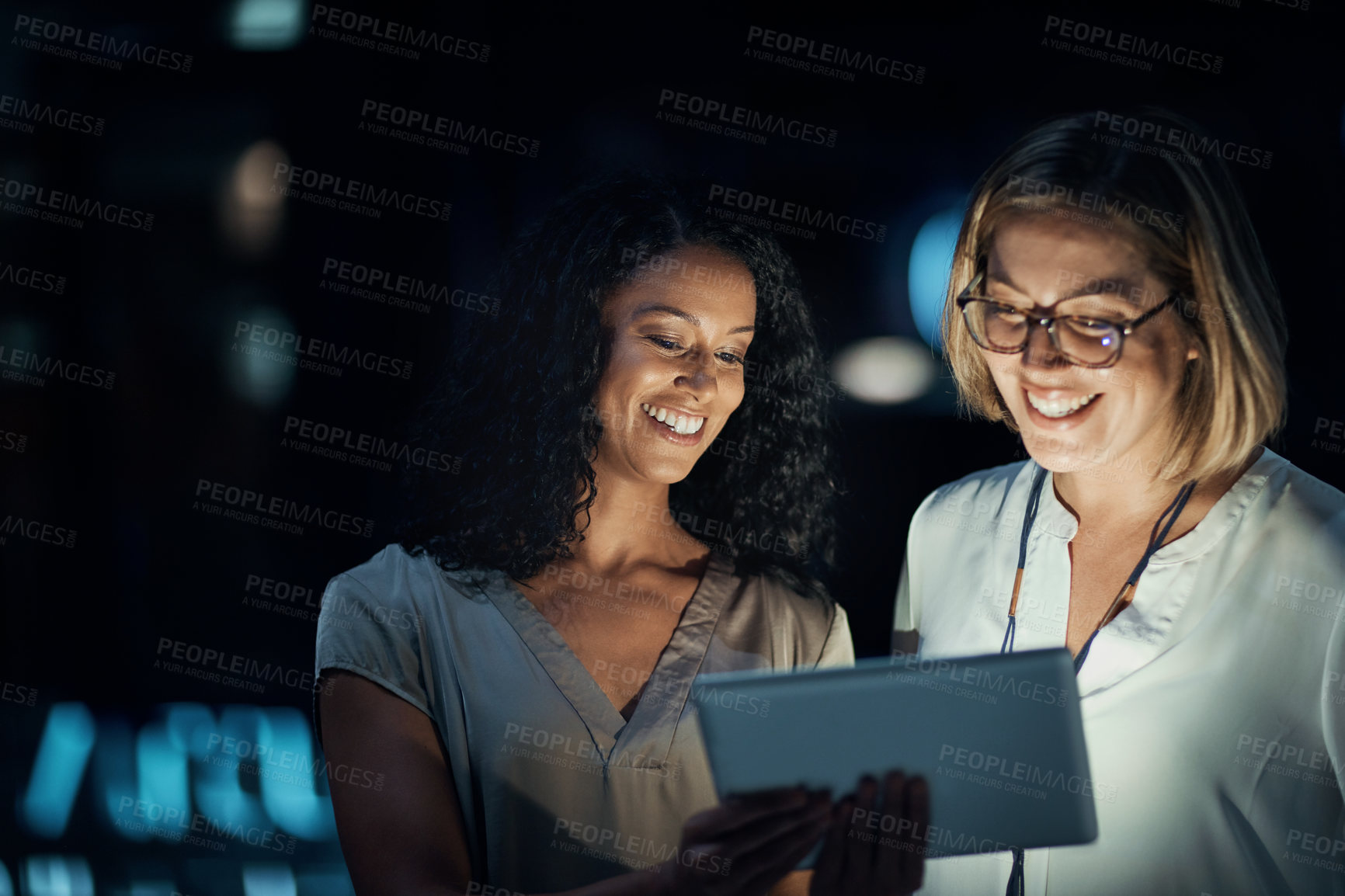 Buy stock photo Shot of two colleagues using a digital tablet together during a late night at work