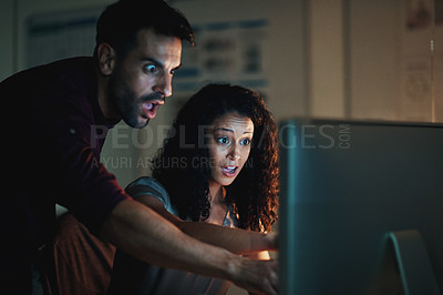 Buy stock photo Shot of two colleagues using a computer together during a late night at work and looking shocked