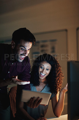 Buy stock photo Shot of two happy colleagues using a digital tablet together during a late night at work