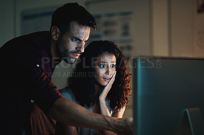 Buy stock photo Shot of two colleagues using a computer together during a late night at work and looking worried