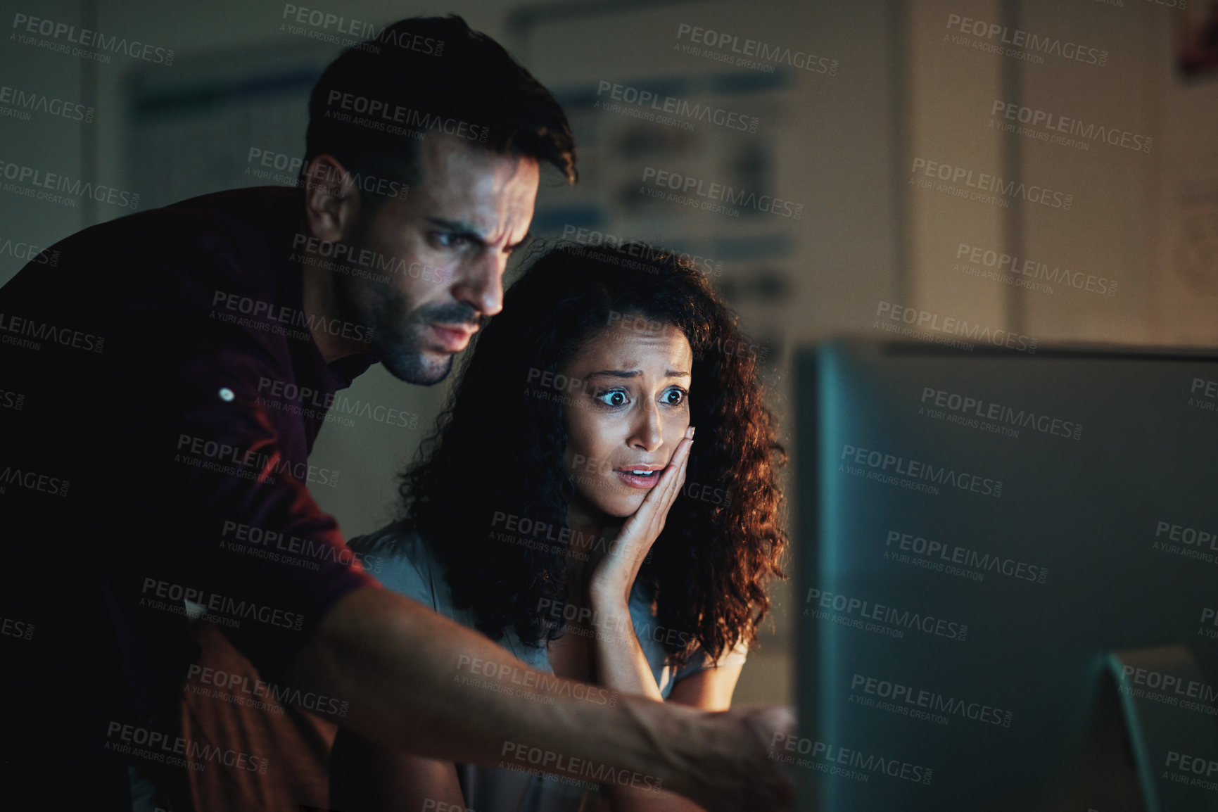 Buy stock photo Shot of two colleagues using a computer together during a late night at work and looking worried