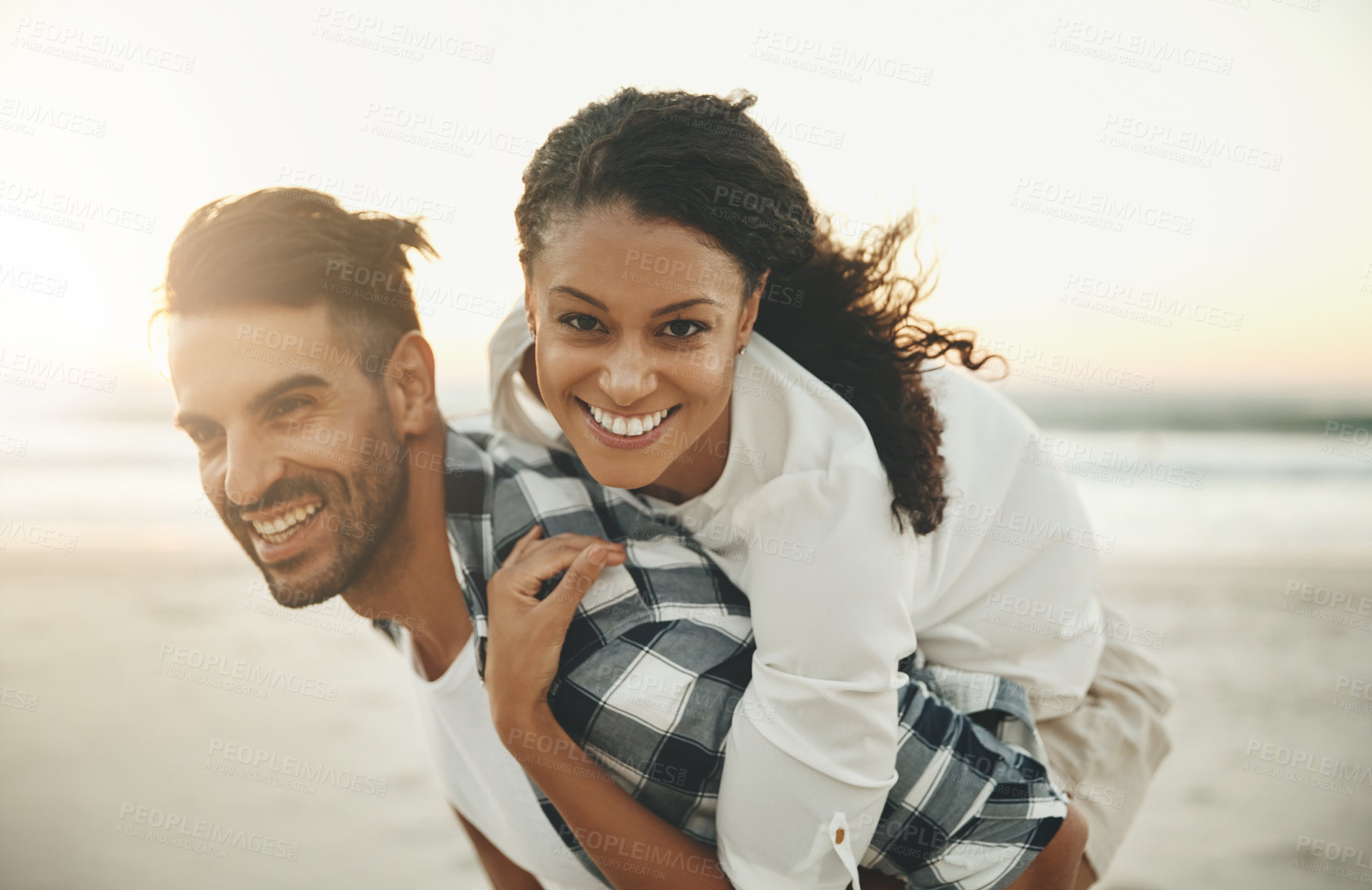 Buy stock photo Shot of a young man piggybacking his girlfriend while spending the day at the beach