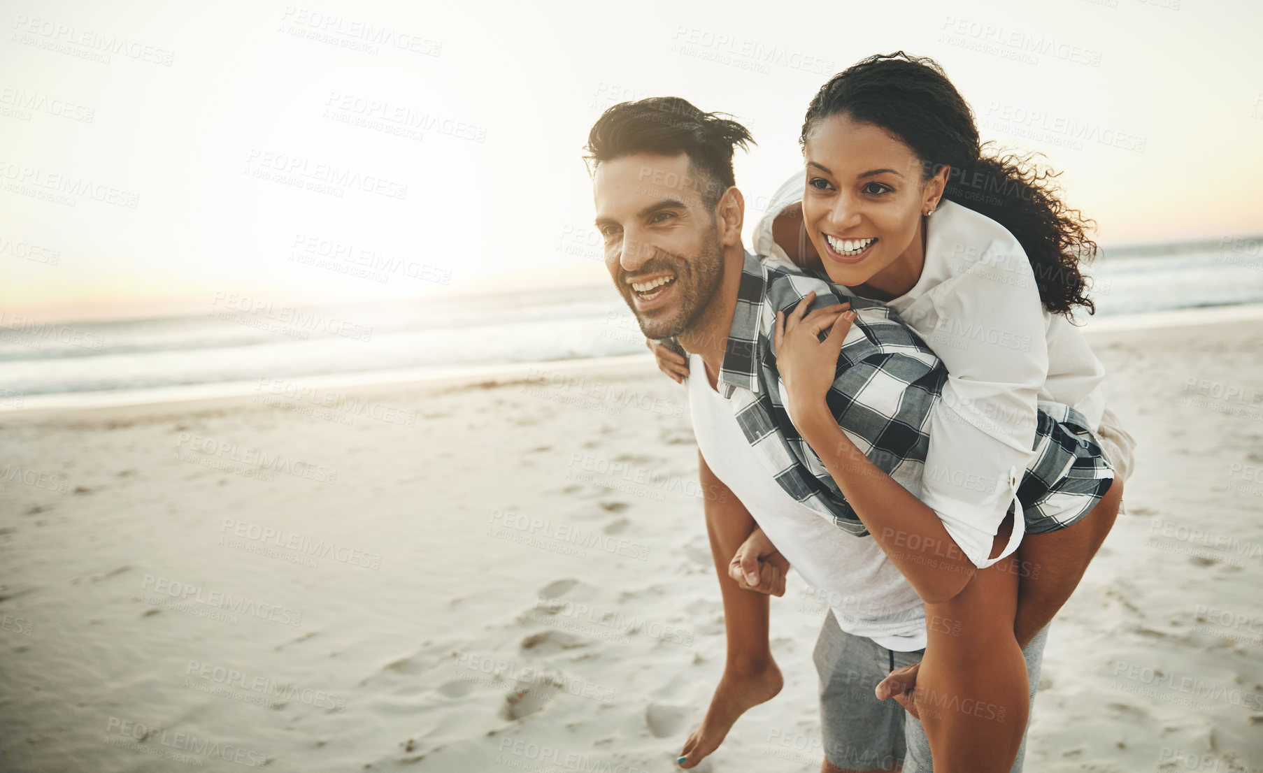 Buy stock photo Shot of a young man piggybacking his girlfriend while spending the day at the beach