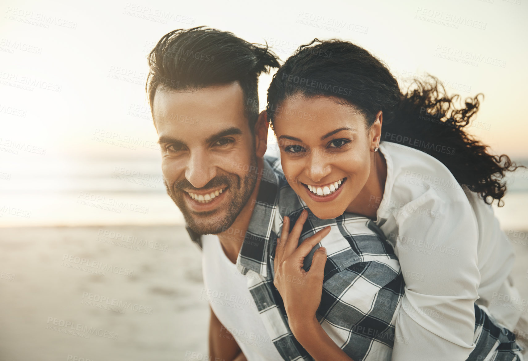 Buy stock photo Shot of a young man piggybacking his girlfriend while spending the day at the beach