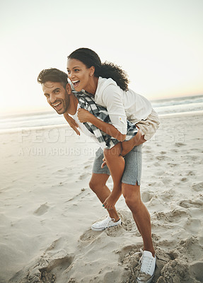 Buy stock photo Shot of a young man piggybacking his girlfriend while spending the day at the beach
