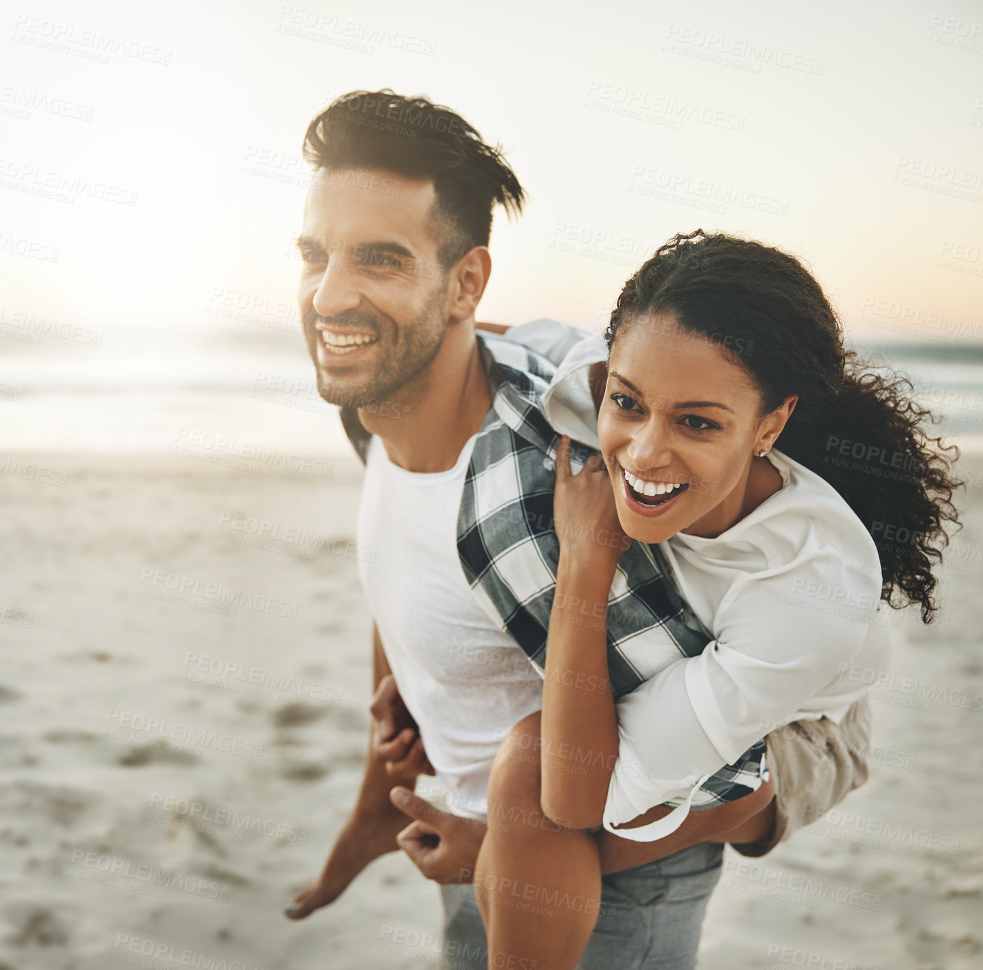 Buy stock photo Shot of a young man piggybacking his girlfriend while spending the day at the beach