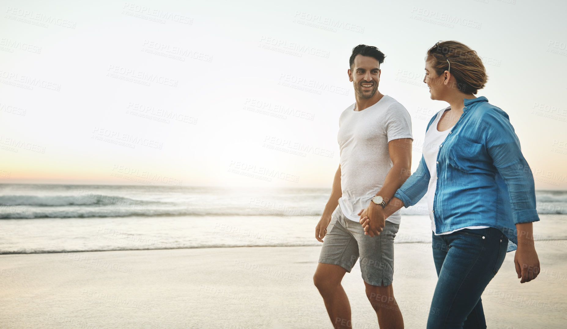 Buy stock photo Shot of a loving couple walking hand in hand on the beach