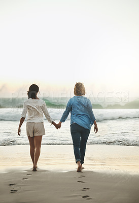 Buy stock photo Rearview shot of a loving couple walking hand in hand on the beach