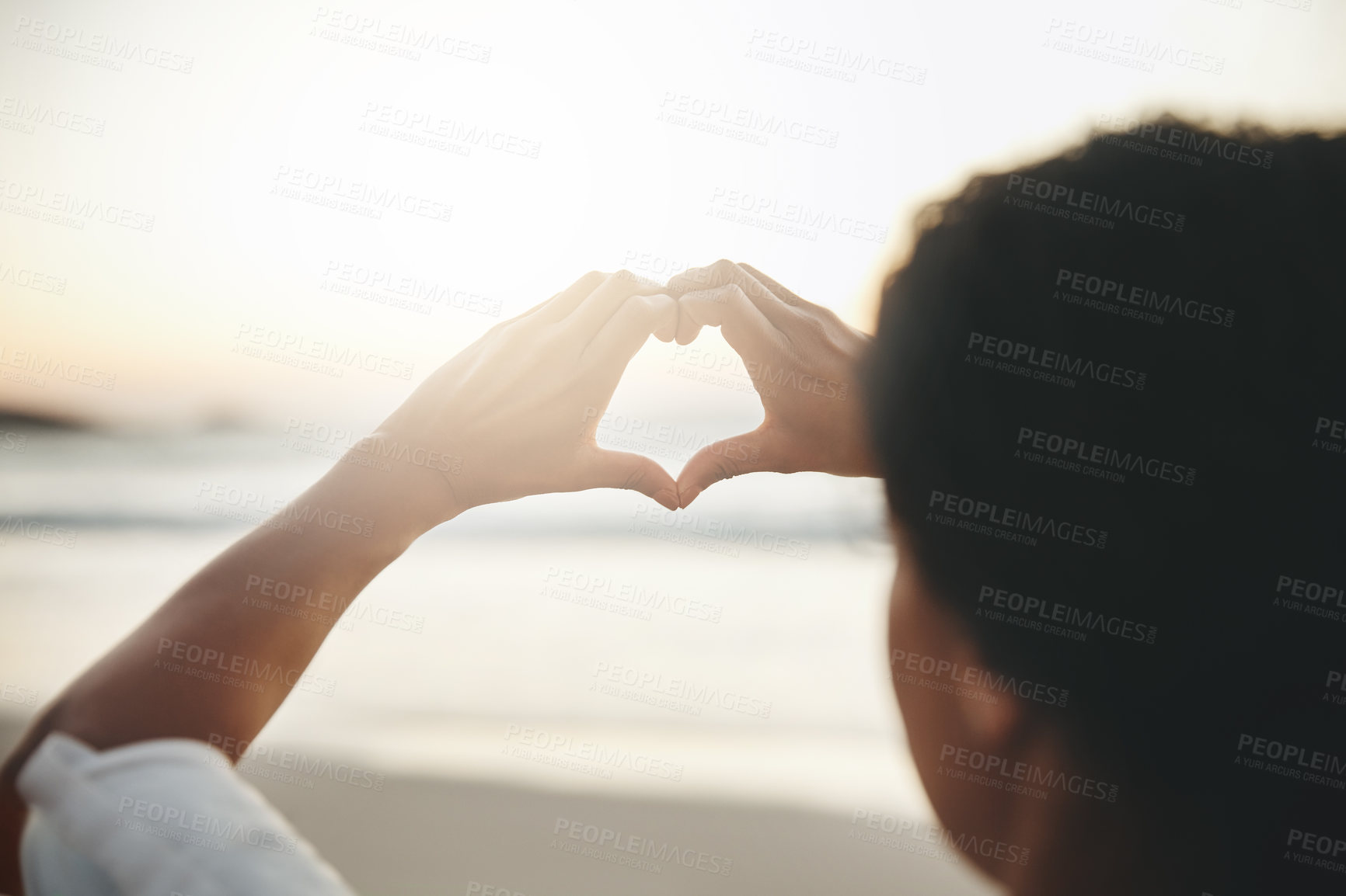 Buy stock photo Rearview shot of a woman woman forming a heart against the horizon at the beach