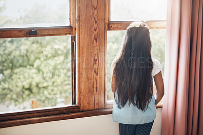 Buy stock photo Rearview shot of a young girl looking out of the window at home