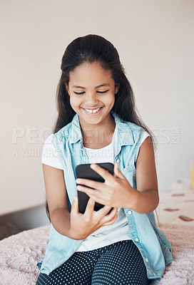 Buy stock photo Shot of a happy young girl sitting on her bed and using a mobile phone at home