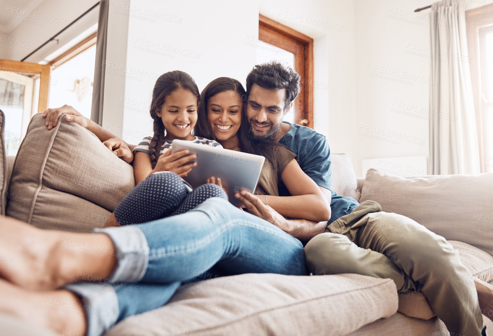 Buy stock photo Shot of a mother and father using a digital tablet with their daughter on the sofa at home