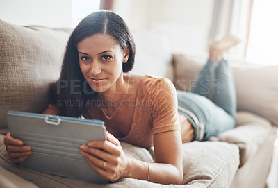 Buy stock photo Shot of a young woman relaxing and using a digital tablet on the sofa at home