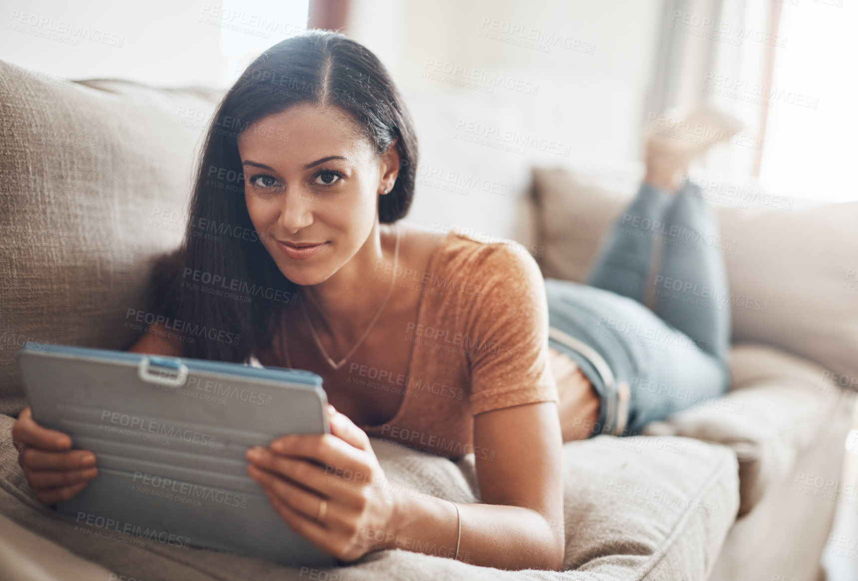 Buy stock photo Shot of a young woman relaxing and using a digital tablet on the sofa at home