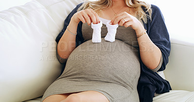 Buy stock photo Shot of an unrecognizable pregnant woman holding baby booties on her belly at home