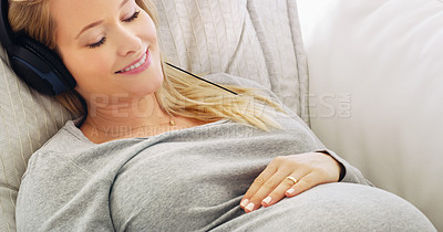 Buy stock photo Shot of a pregnant woman listening to music with headphones at home
