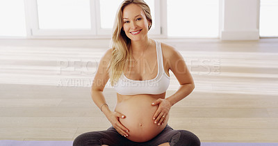 Buy stock photo Cropped portrait of an attractive young pregnant woman rubbing her baby bump while sitting on a yoga mat