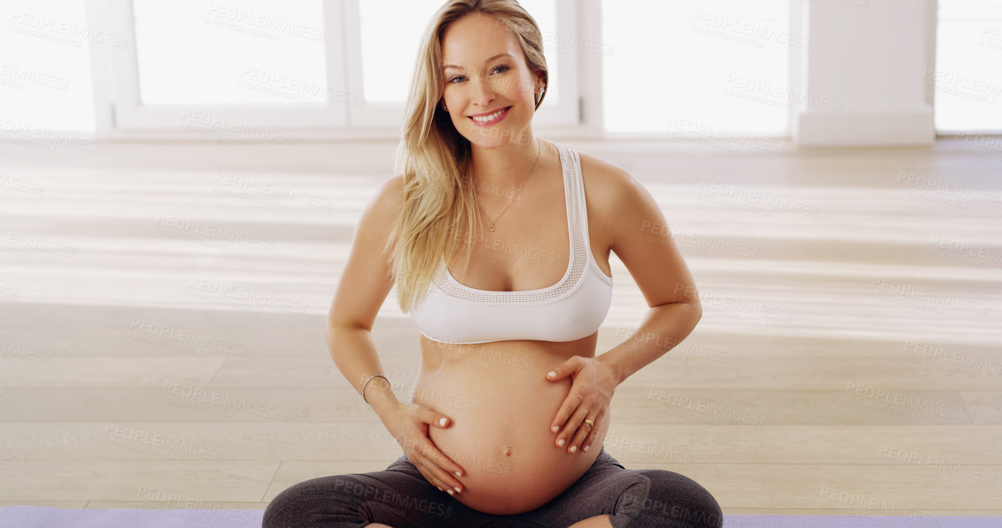 Buy stock photo Cropped portrait of an attractive young pregnant woman rubbing her baby bump while sitting on a yoga mat