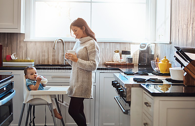 Buy stock photo Shot of an adorable baby girl drinking bottled milk in her high chair while her mother has coffee