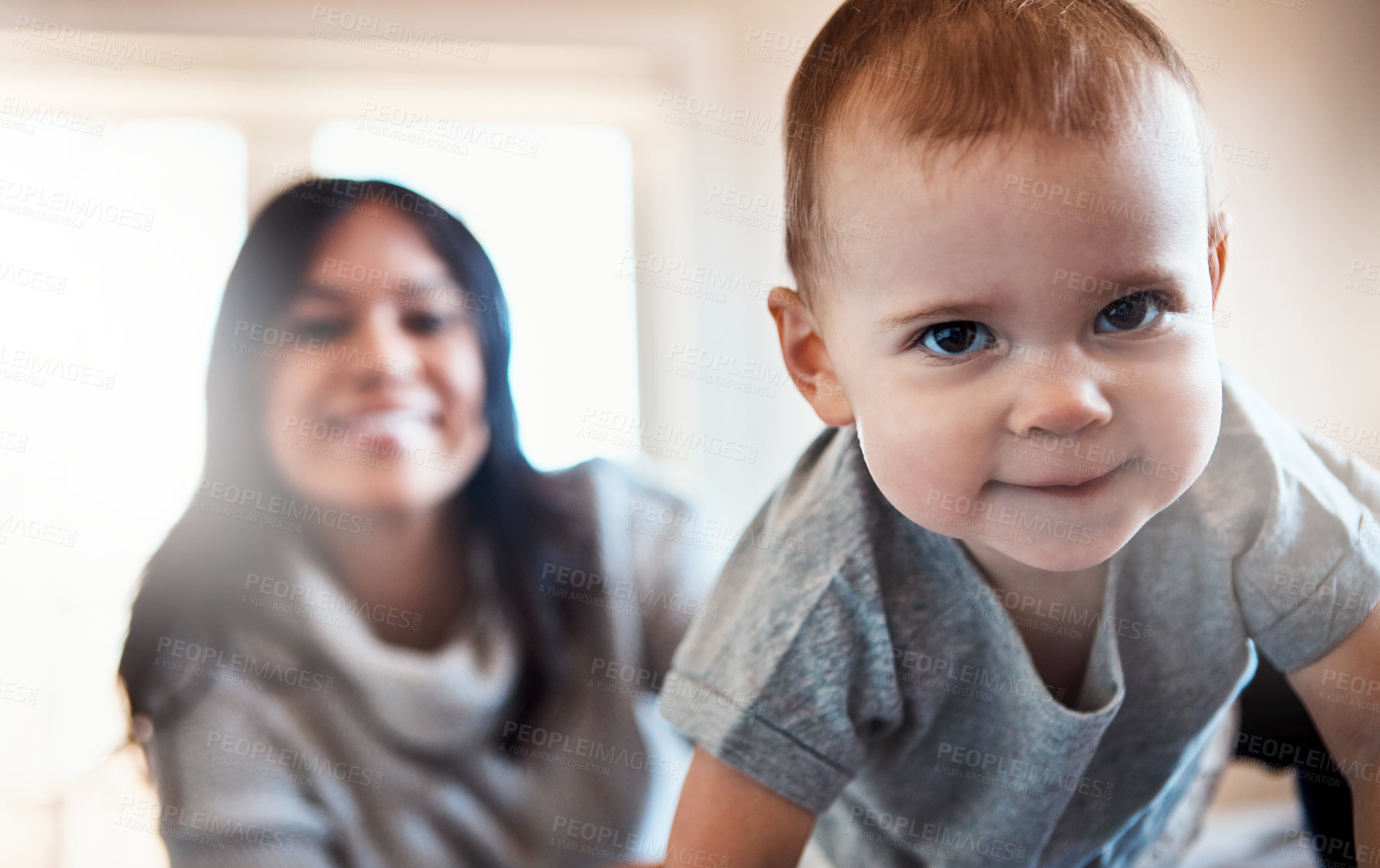 Buy stock photo Shot of an adorable baby girl crawling on a bed with her mother in the background