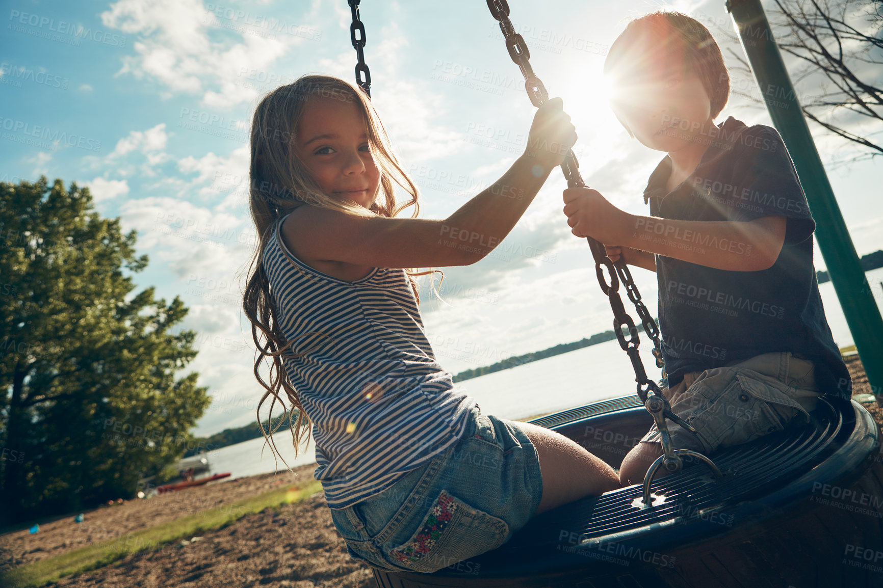 Buy stock photo Children, tire swing and portrait in outdoor, bonding and friends at playground for game or adventure. Kids, lens flare and together for fun in backyard or freedom, play and connection on vacation