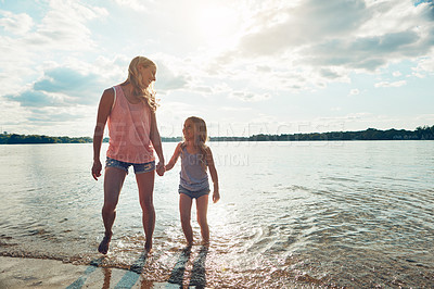 Buy stock photo Shot of mother and daughter playing in the water by a lake outdoors