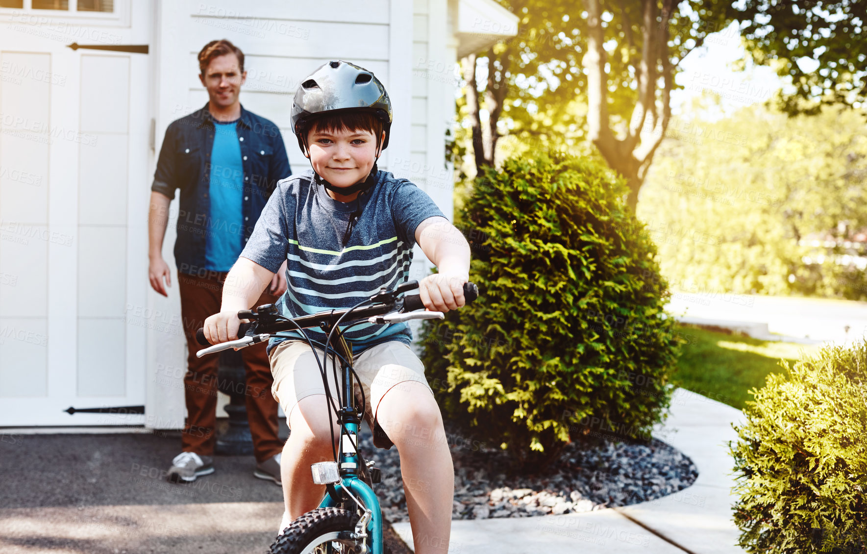 Buy stock photo Shot of a young boy riding a bicycle with his father in the background