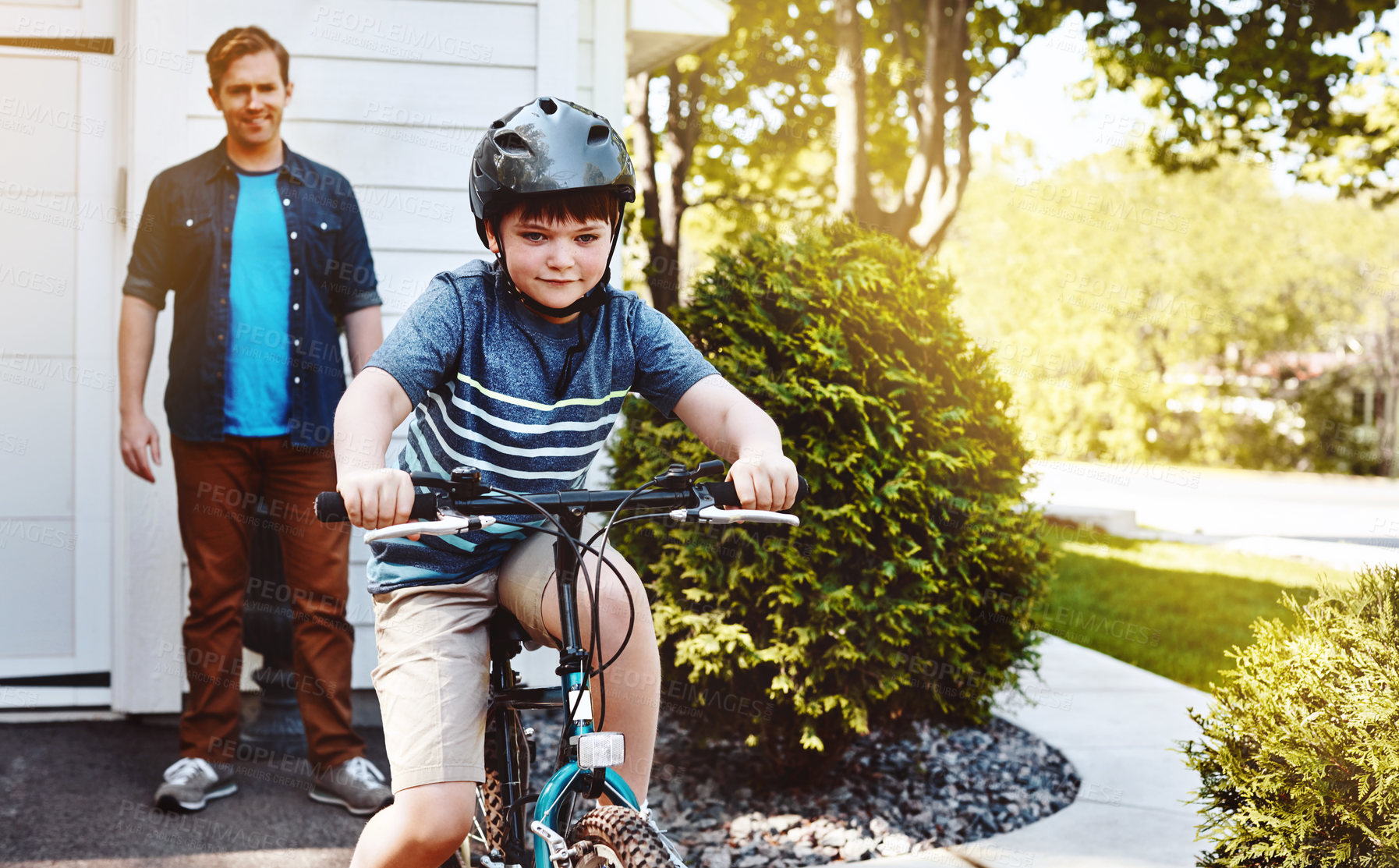 Buy stock photo Shot of a young boy riding a bicycle with his father in the background