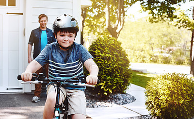 Buy stock photo Shot of a young boy riding a bicycle with his father in the background