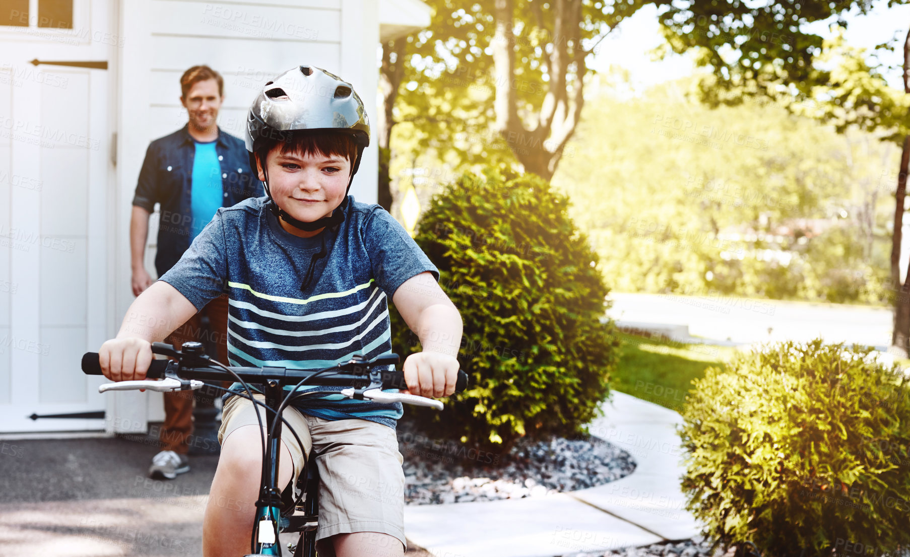 Buy stock photo Shot of a young boy riding a bicycle with his father in the background