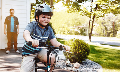 Buy stock photo Shot of a young boy riding a bicycle with his father in the background