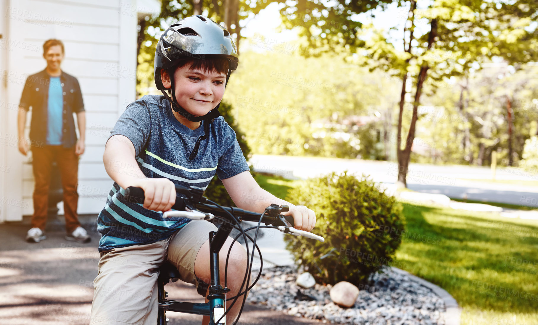 Buy stock photo Shot of a young boy riding a bicycle with his father in the background