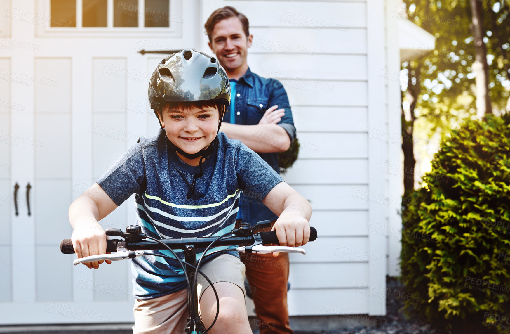 Buy stock photo Shot of a young boy riding a bicycle with his father in the background